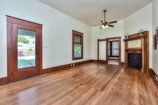 unfurnished living room featuring a barn door, ceiling fan, wood-type flooring, and vaulted ceiling