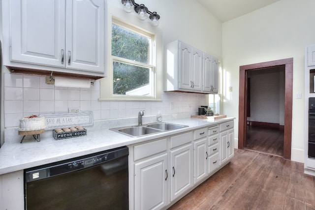 kitchen featuring black dishwasher, tasteful backsplash, white cabinets, wood finished floors, and a sink