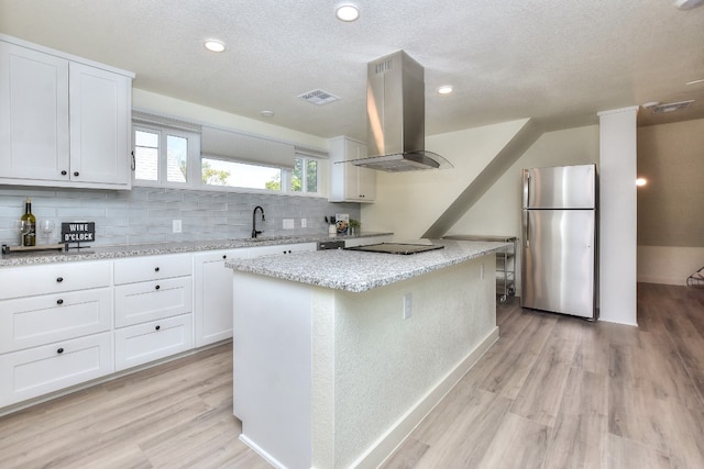 kitchen with light wood-type flooring, stainless steel fridge, white cabinets, and island range hood