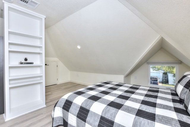 bedroom with a textured ceiling, vaulted ceiling, and light wood-type flooring