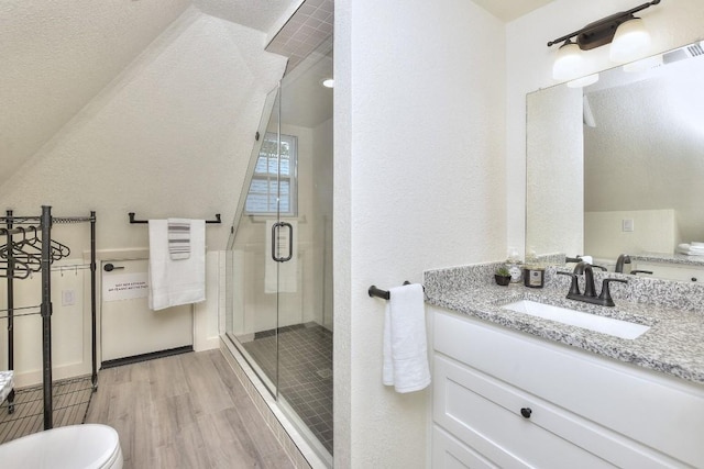 bathroom with a textured wall, toilet, wood finished floors, vanity, and a stall shower