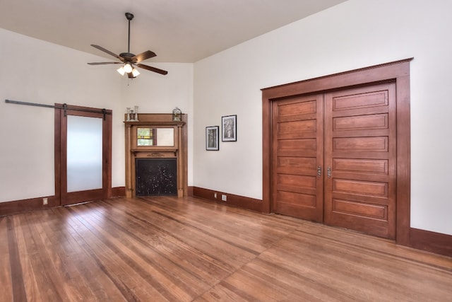 unfurnished living room featuring a fireplace, ceiling fan, baseboards, and wood finished floors