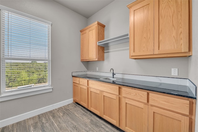 kitchen featuring dark stone counters, light brown cabinetry, wood-type flooring, and sink