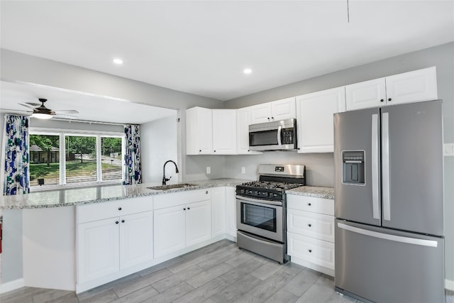 kitchen with light stone counters, kitchen peninsula, sink, ceiling fan, and appliances with stainless steel finishes