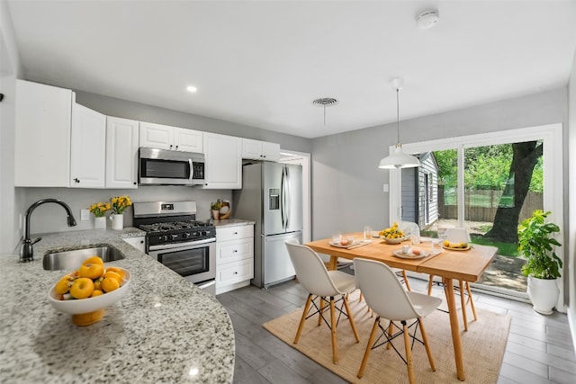 kitchen with light stone counters, sink, appliances with stainless steel finishes, hardwood / wood-style flooring, and white cabinets