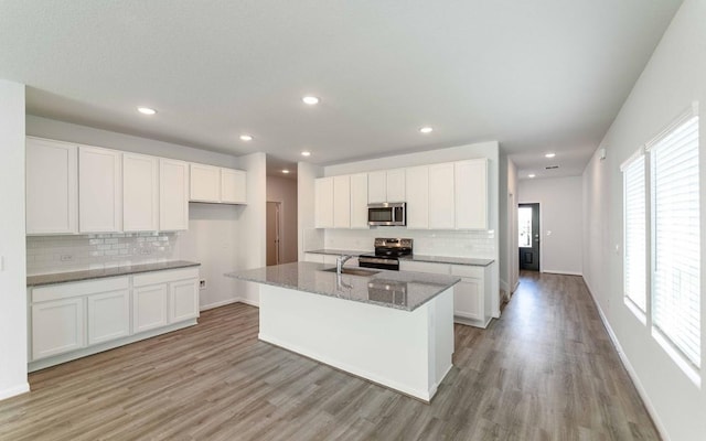 kitchen with light stone counters, light hardwood / wood-style flooring, a center island with sink, white cabinets, and appliances with stainless steel finishes