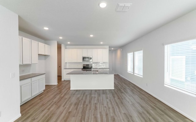 kitchen with white cabinets, light hardwood / wood-style flooring, stainless steel appliances, and an island with sink