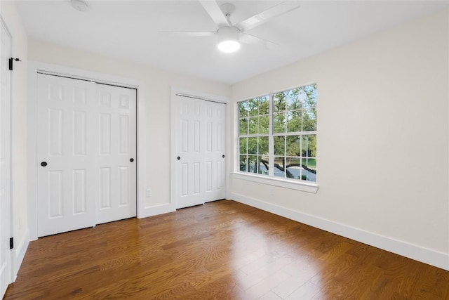 unfurnished bedroom featuring hardwood / wood-style flooring, ceiling fan, and multiple closets