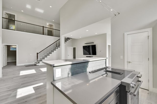 kitchen featuring a towering ceiling, stainless steel electric range oven, and light hardwood / wood-style floors