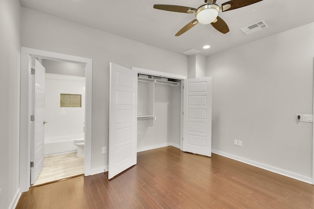 unfurnished bedroom featuring ensuite bath, hardwood / wood-style flooring, ceiling fan, and a closet