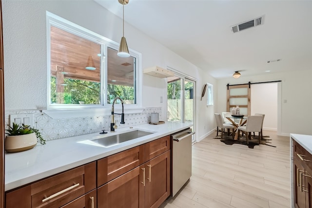 kitchen featuring light wood-type flooring, tasteful backsplash, dishwasher, sink, and hanging light fixtures