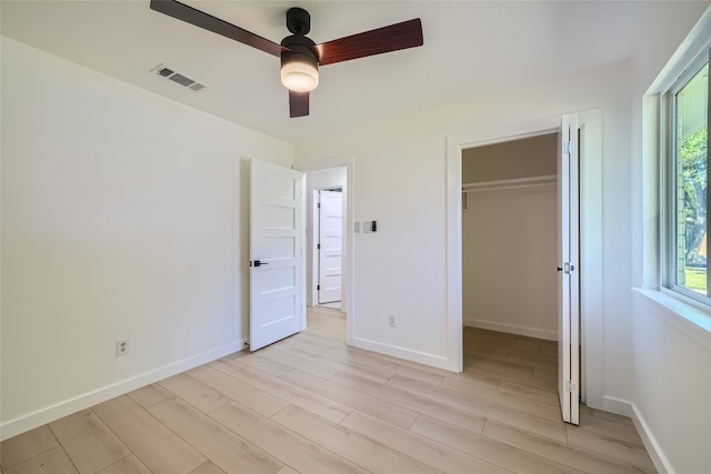 unfurnished bedroom featuring light hardwood / wood-style floors, a walk in closet, ceiling fan, and a closet