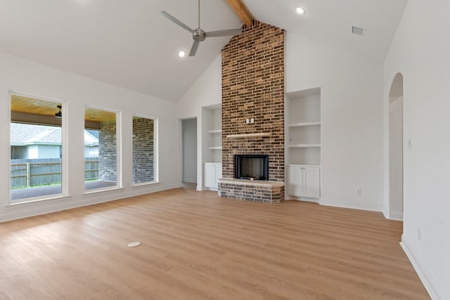 unfurnished living room featuring a fireplace, light hardwood / wood-style flooring, ceiling fan, high vaulted ceiling, and beam ceiling