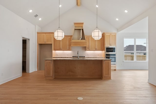 kitchen featuring light wood-type flooring, appliances with stainless steel finishes, high vaulted ceiling, and a kitchen island with sink