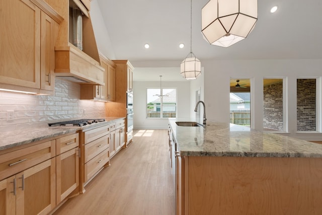 kitchen with light hardwood / wood-style flooring, decorative light fixtures, ceiling fan, decorative backsplash, and a center island with sink