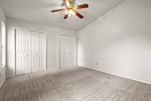 unfurnished bedroom featuring lofted ceiling, ceiling fan, carpet floors, and multiple closets