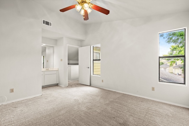 unfurnished bedroom featuring light carpet, multiple windows, connected bathroom, and ceiling fan