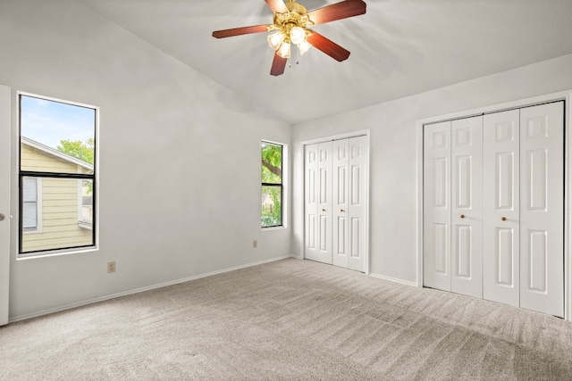 unfurnished bedroom featuring two closets, light colored carpet, ceiling fan, and vaulted ceiling