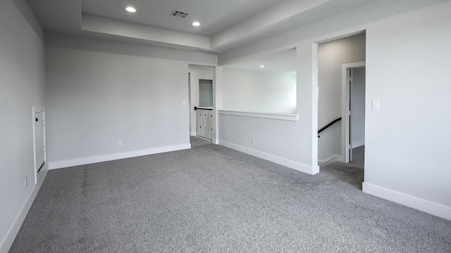 empty room featuring dark colored carpet and a tray ceiling