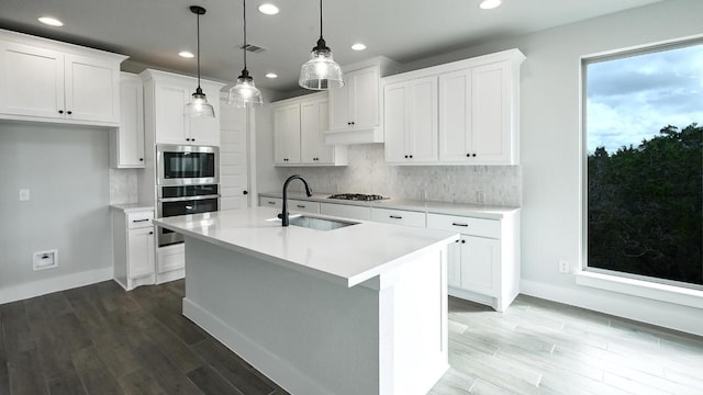 kitchen with sink, an island with sink, appliances with stainless steel finishes, decorative light fixtures, and white cabinetry