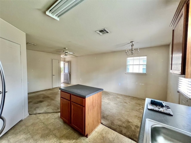 kitchen featuring light carpet, ceiling fan with notable chandelier, a textured ceiling, decorative light fixtures, and a center island