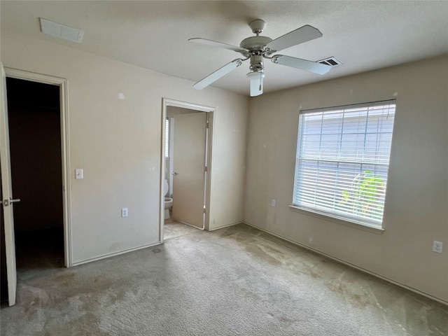 unfurnished bedroom with ceiling fan, ensuite bathroom, light colored carpet, a walk in closet, and a closet