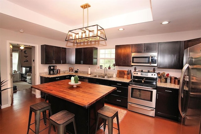 kitchen with recessed lighting, stainless steel appliances, a sink, a kitchen breakfast bar, and wooden counters