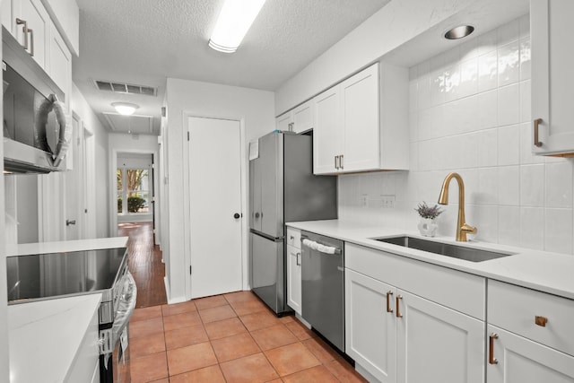 kitchen with white cabinets, appliances with stainless steel finishes, sink, light tile patterned flooring, and a textured ceiling