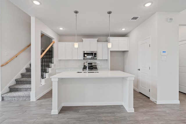 kitchen featuring appliances with stainless steel finishes, light countertops, visible vents, and an island with sink