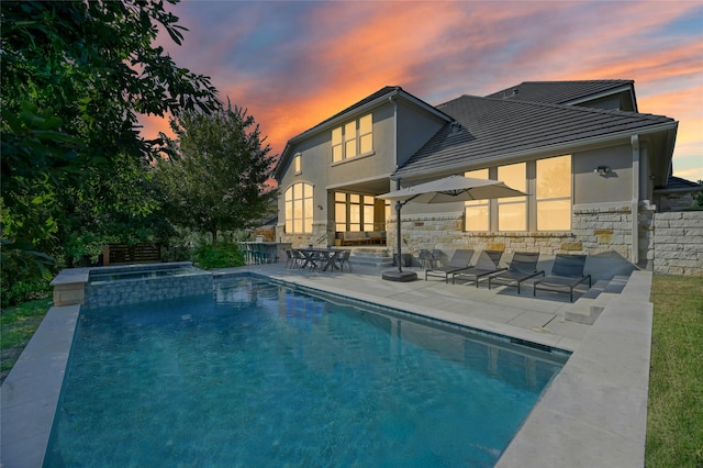 back house at dusk with a pool with hot tub and a patio