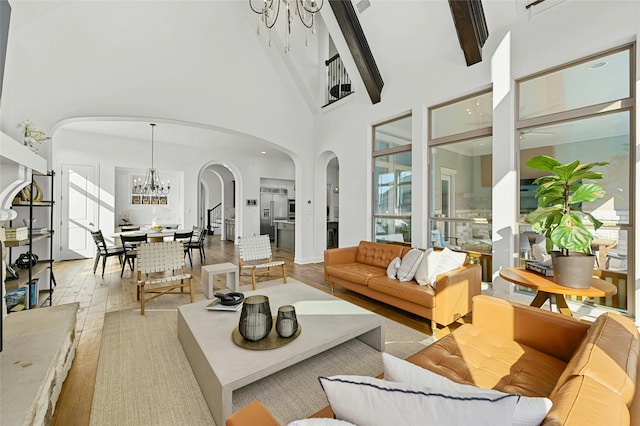 living room with a towering ceiling, beamed ceiling, an inviting chandelier, and light hardwood / wood-style floors