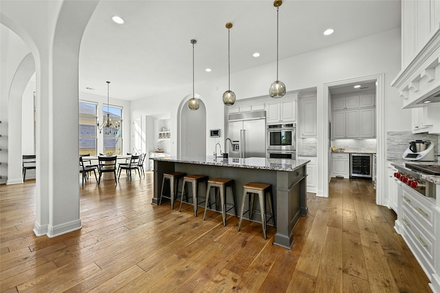 kitchen with wine cooler, a spacious island, decorative backsplash, hanging light fixtures, and appliances with stainless steel finishes