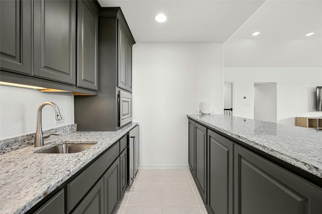 kitchen with stainless steel microwave, light tile patterned floors, light stone countertops, and sink