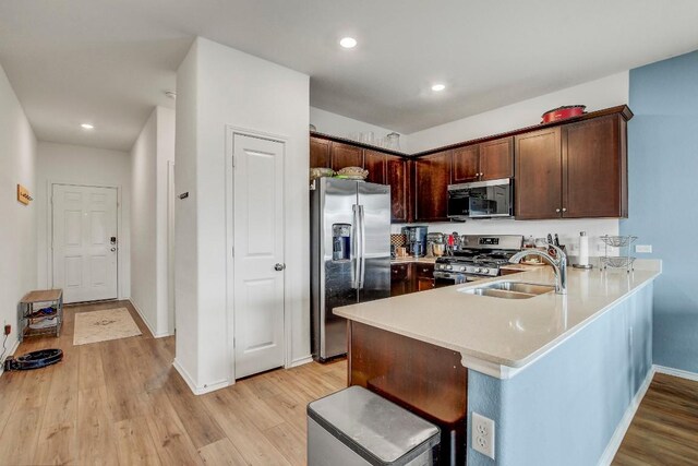 kitchen with light hardwood / wood-style flooring, stainless steel appliances, sink, kitchen peninsula, and dark brown cabinetry