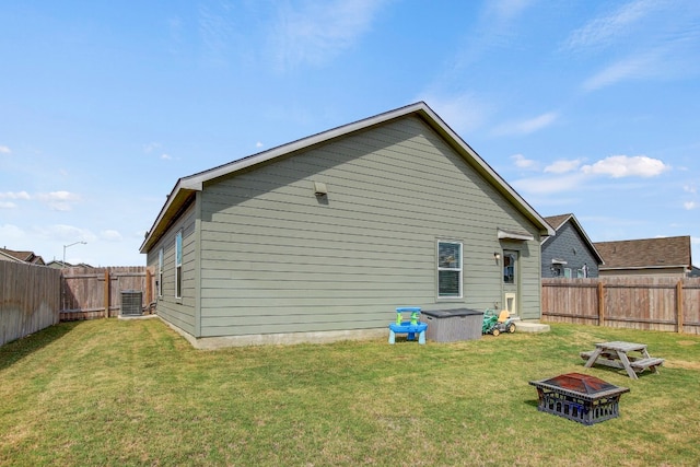 rear view of house featuring a fire pit, central air condition unit, and a yard