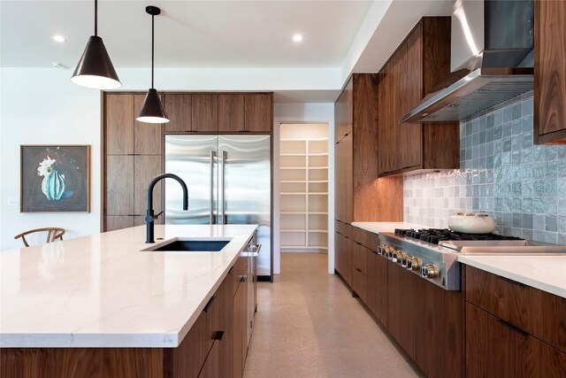 kitchen with backsplash, light stone countertops, stainless steel appliances, wall chimney range hood, and a kitchen island with sink