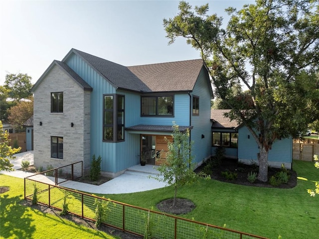 rear view of house with roof with shingles, a lawn, fence private yard, and board and batten siding