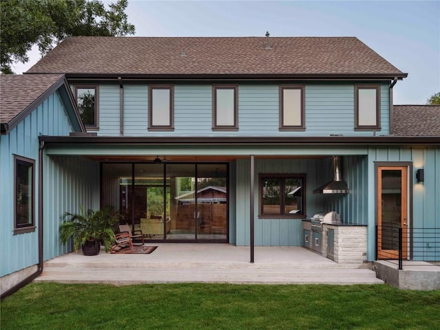 back of property with a shingled roof, a lawn, exterior kitchen, a patio area, and board and batten siding