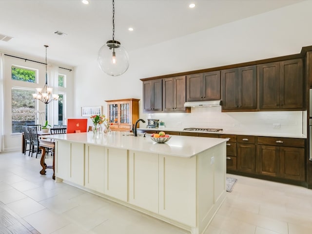 kitchen featuring hanging light fixtures, stainless steel gas cooktop, a chandelier, decorative backsplash, and a center island with sink