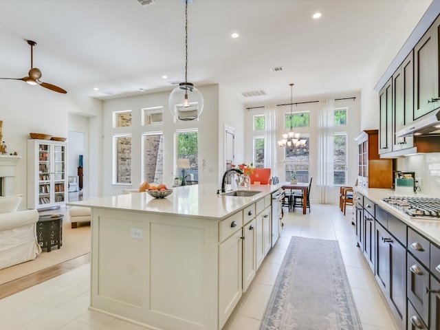 kitchen featuring sink, tasteful backsplash, pendant lighting, stainless steel gas stovetop, and a center island with sink