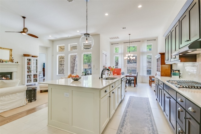 kitchen with decorative backsplash, stainless steel gas cooktop, sink, hanging light fixtures, and an island with sink