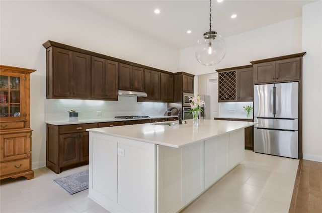 kitchen with sink, stainless steel appliances, pendant lighting, decorative backsplash, and a center island with sink