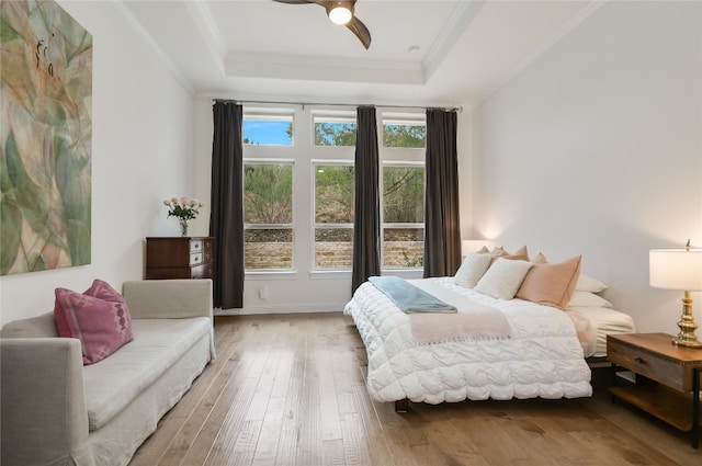 bedroom with a raised ceiling, ceiling fan, hardwood / wood-style floors, and crown molding