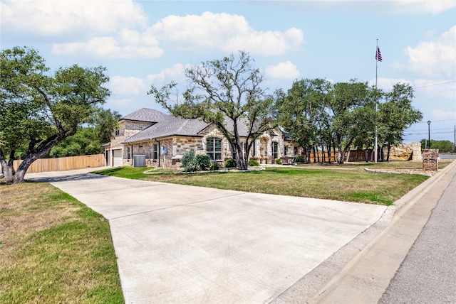 view of front of home with concrete driveway, fence, a front lawn, and stone siding