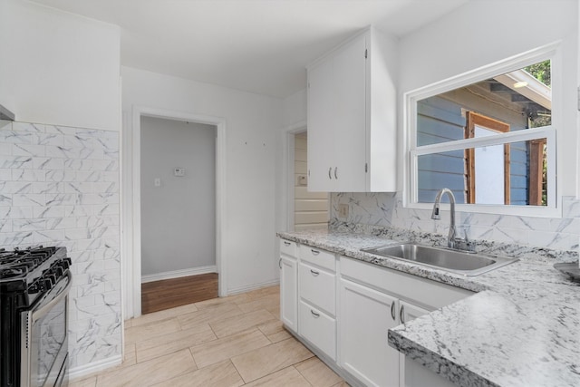 kitchen with white cabinetry, light hardwood / wood-style flooring, stainless steel gas range oven, backsplash, and sink