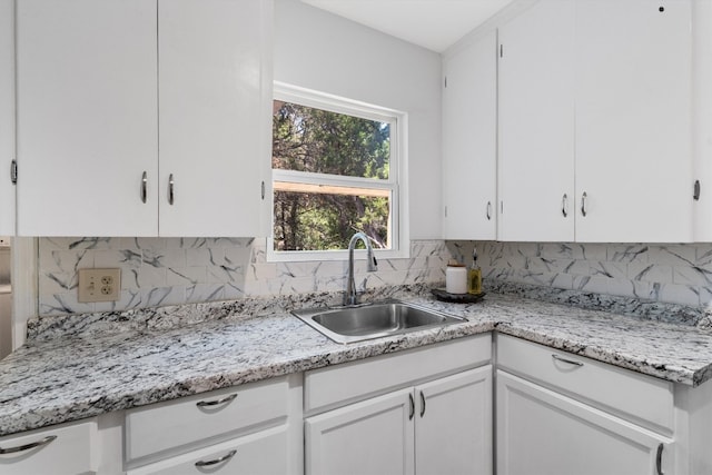 kitchen with white cabinets, light stone countertops, tasteful backsplash, and sink