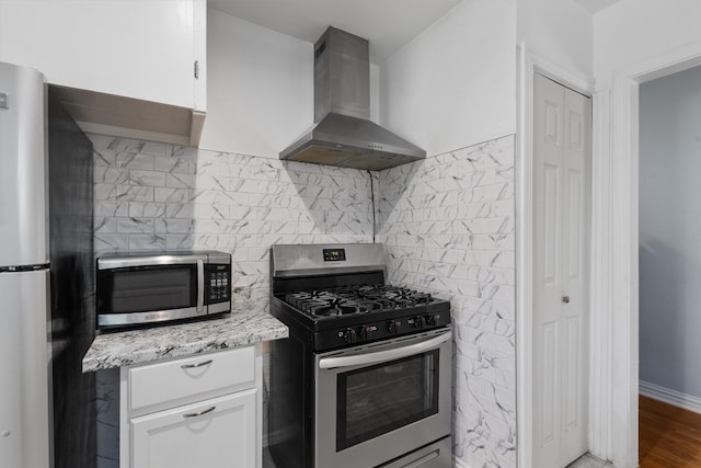 kitchen with white cabinets, backsplash, stainless steel appliances, wall chimney range hood, and wood-type flooring