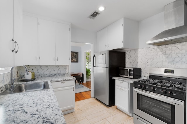 kitchen featuring light wood-type flooring, stainless steel appliances, sink, decorative backsplash, and wall chimney range hood