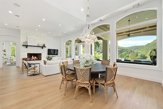 dining room with light wood-type flooring, a stone fireplace, and a notable chandelier