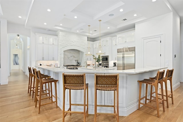 kitchen with a kitchen breakfast bar, built in appliances, white cabinetry, and light hardwood / wood-style floors